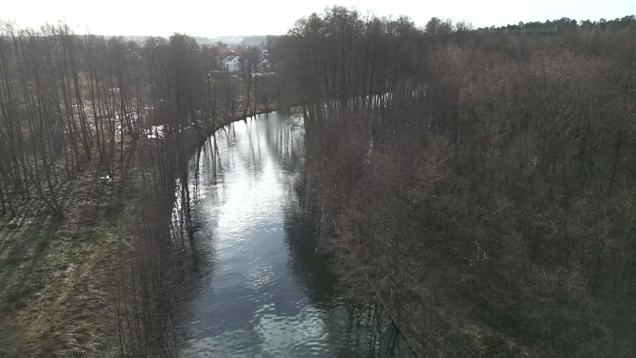 Droneoverflyvning over en kunstigt anlagt kanal omgivet af tørre træer.