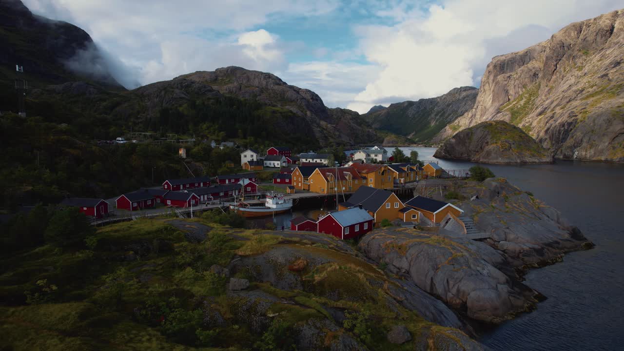 Coastal town in Norway with red and yellow wooden rorbuer cabins, clear sea water, and dramatic cliffs