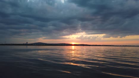 the setting sun hides behind the hill. cumulus clouds in the sky. sunset colors the horizon in yellow and pink.  a light wind forms waves on the water surface