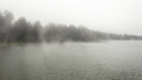 Aerial-view-backwards-through-fog-clouds-on-a-misty-marsh,-cloudy-day-in-USA