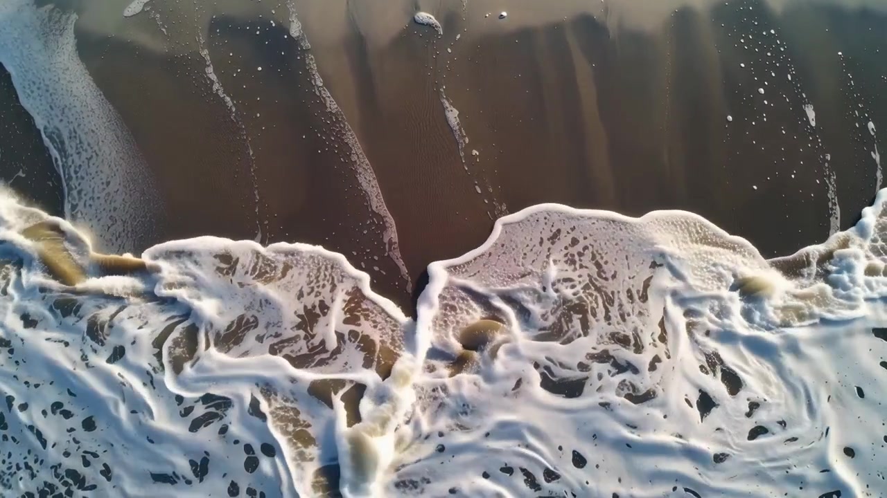 Aerial Top-Down View of Ocean Waves Crashing on Sandy Beach with Foaming Water