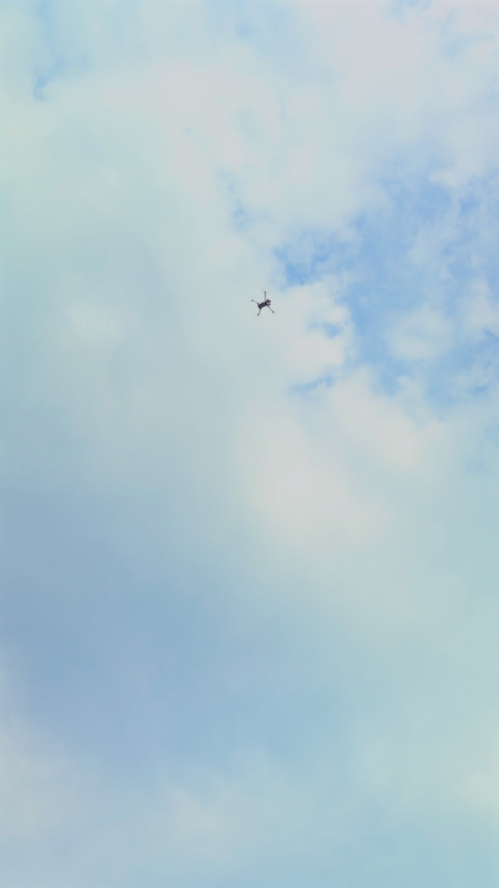 Vertical shot of a drone ascending into the sky on a partly cloudy day, showcasing aerial technology and smooth upward movement through soft light and open air