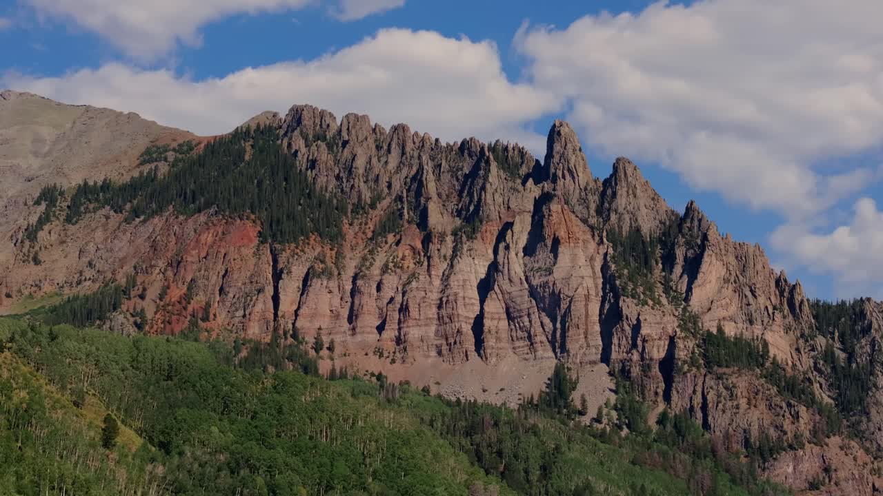 Scogliere frastagliate di roccia rossa si ergono sopra la foresta verde in un drammatico paesaggio montano, Autostrada 145 Colorado USA.