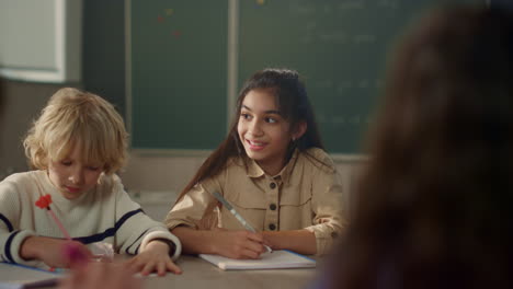 Students-learning-at-round-table-in-school.-Pupils-writing-text-in-notebooks