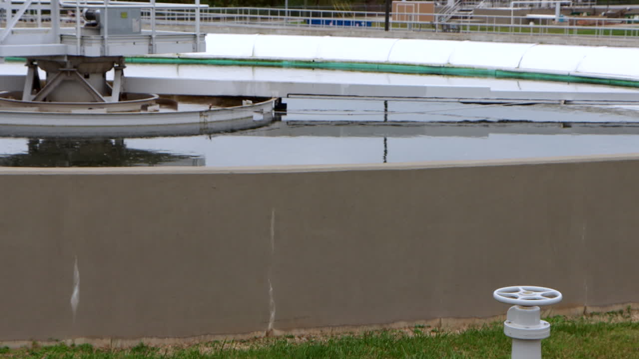 A clarifying pool at the wastewater treatment plant gently processes water, its surface slowly moving as sediments settle in a calm, industrial purification scene