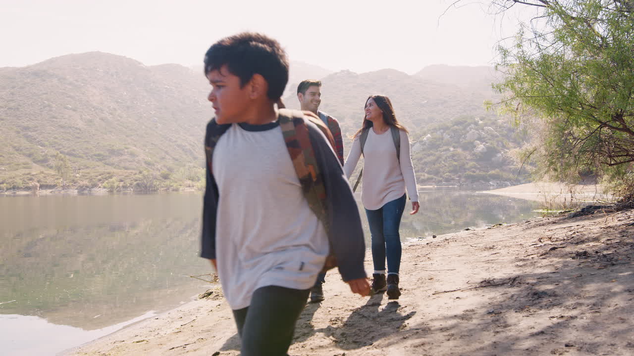 어린 가족 이 산 에 있는 호수 를 따라 산책 하고 있다