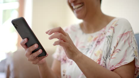 Happy-senior-biracial-woman-sitting-on-couch-and-talking-on-smartphone-at-home,-slow-motion