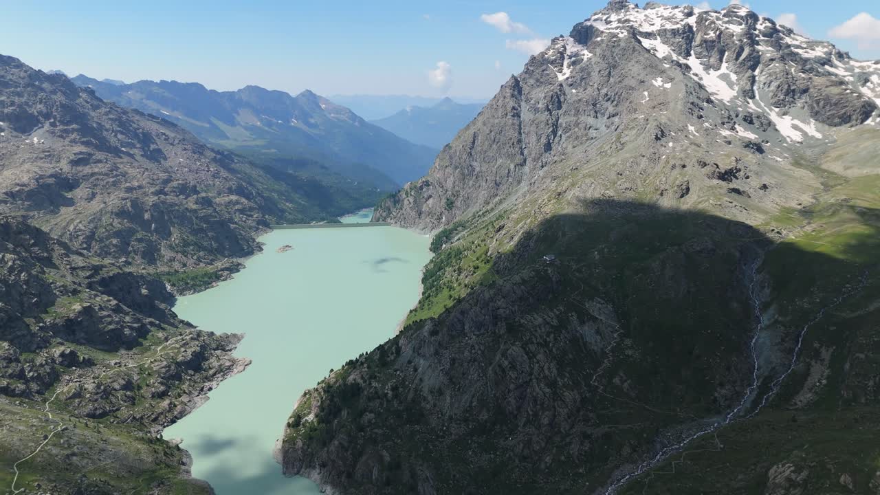 Zoom su riprese aeree che catturano un lago glaciale verde pallido alla base del ghiacciaio Fellaria, circondato da ripidi pendii alpini