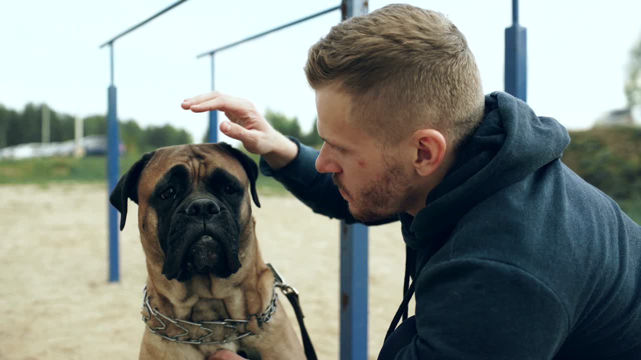 젊은 스포츠 남자가 자연에서 야외에서 그의 불마스티프 개를 포옹하고 놀고 있습니다.