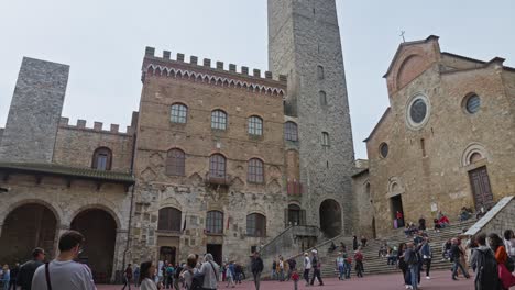 several tourists at the famous piazza del duomo in the historic town of san gimignano, tuscany, italy