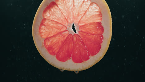 Grapefruit-Scheibe,-Die-Von-Wassertropfennebel-Mit-Flüssigkeitstropfen-In-Zeitlupe-Mit-Hintergrundbeleuchtung-Auf-Schwarzem-Hintergrund-Bespritzt-Wird