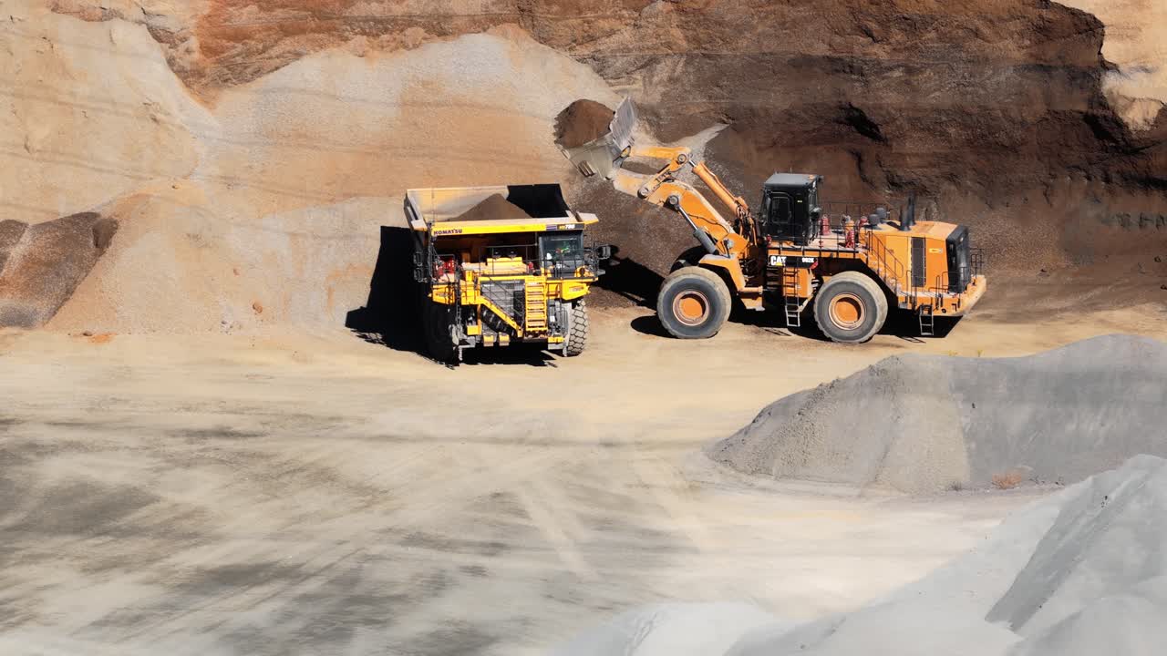 Wheel loader filling dump truck with gravel at quarry, aerial overview of full process