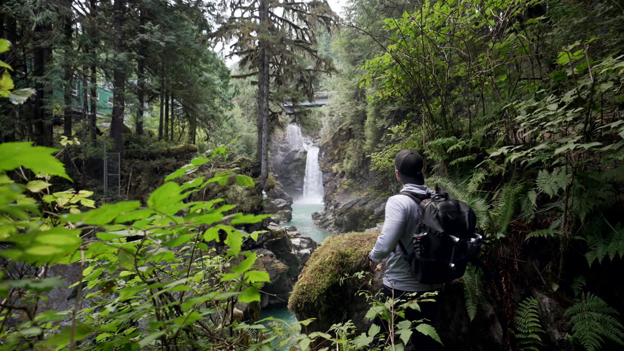 excursionista masculino camina en el bosque con vista panorámica de las cataratas mamquam en squamish, bc, canadá
