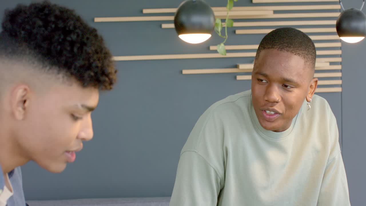 Two male friends sitting on sofa, left man speaking to discuss ideas after reading paper, nodding