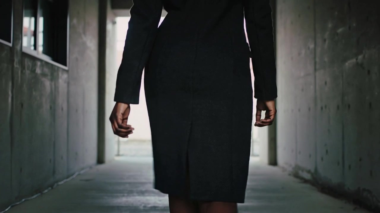 Walking woman in black dress moving toward opening in concrete passage, light drawing her forward
