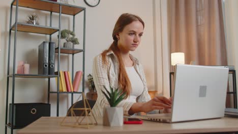 young woman girl using laptop computer sitting at table working online shopping from home office
