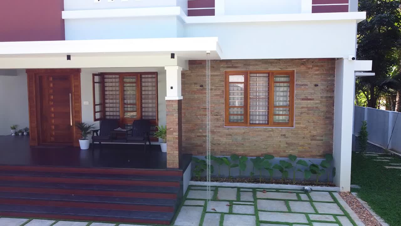 Stunning Kerala home in India with modern architecture, brick exterior, and lush garden. Features a cozy porch, wooden windows, stone pathway, and green lawn. Ideal for real estate, travel,