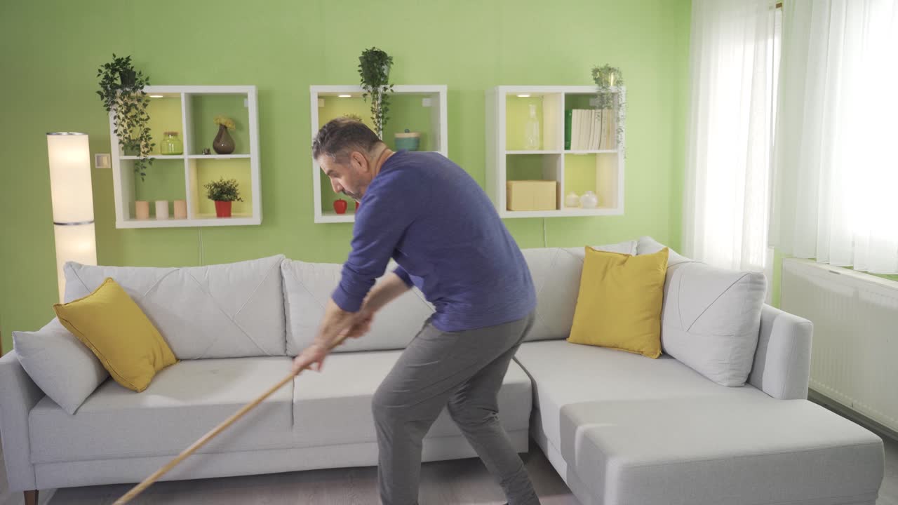 hombre maduro limpiando el suelo con un trapeador en la sala de estar en casa y cansándose.