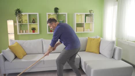 hombre maduro limpiando el suelo con un trapeador en la sala de estar en casa y cansándose.