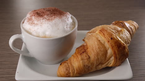 pouring cocoa on cappuccino milk coffee and brioche croissant breakfast