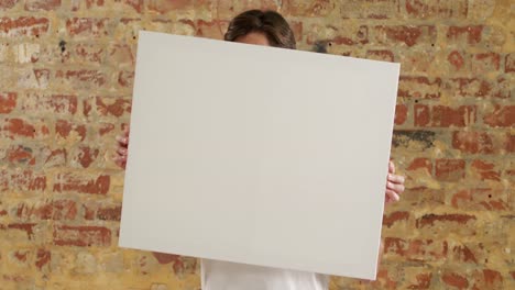 caucasian man holding a white rectangle on a brick wall