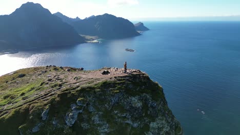 Orbiting-aerial-view-of-two-persons-orbiting-in-Lofoten,-Norway-with-views-of-many-surrounding-mountains-and-fjords