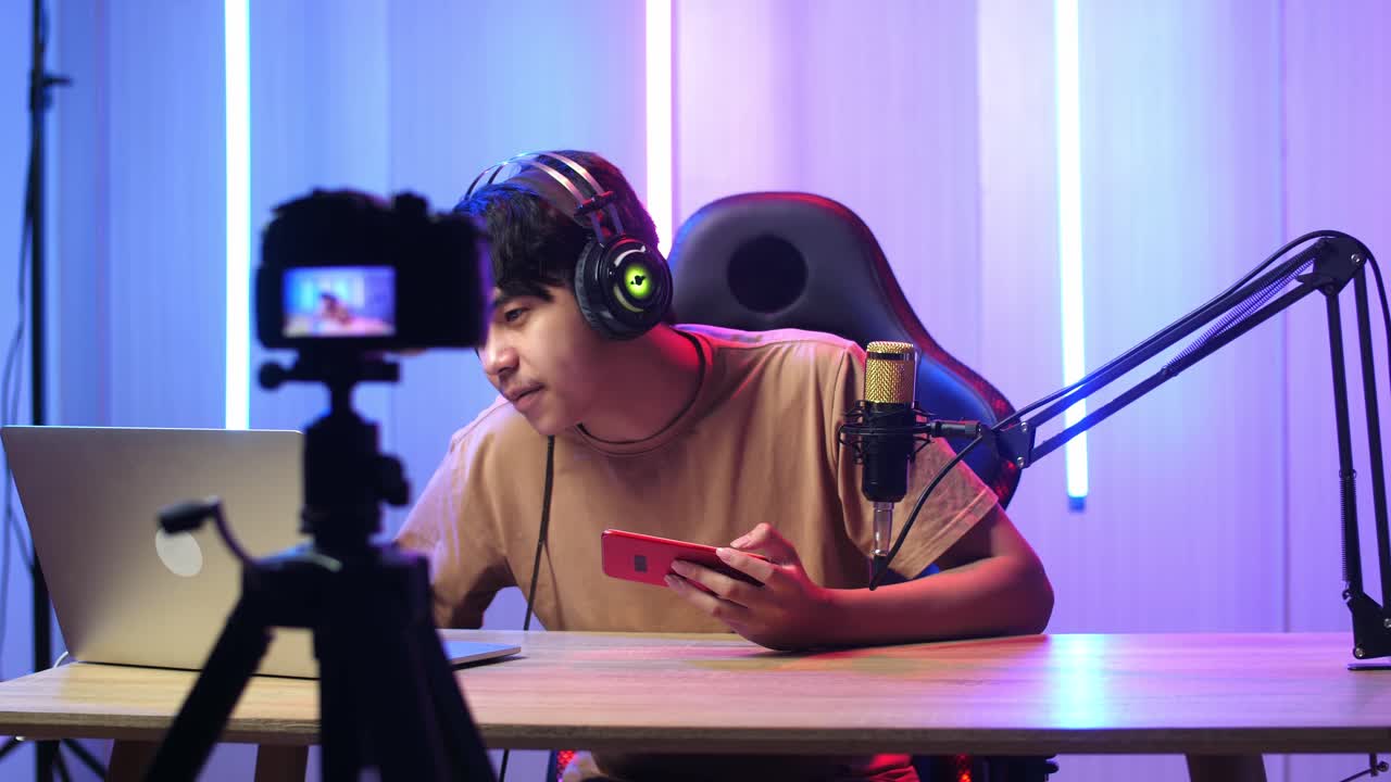 Asian Man Holding Mobile Phone And Read Comment In Laptop Computer Then Talking To Camera While Live Stream