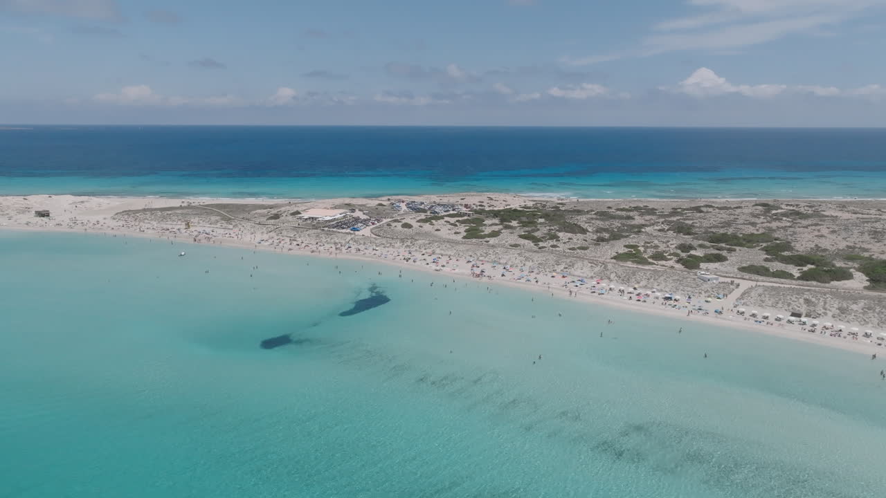 Lento drone che si allontana dalle barche ancorate nelle acque cristalline turchesi di Ses Illetes, rivelando i banchi di sabbia e la costa poco profonda di Formentera
