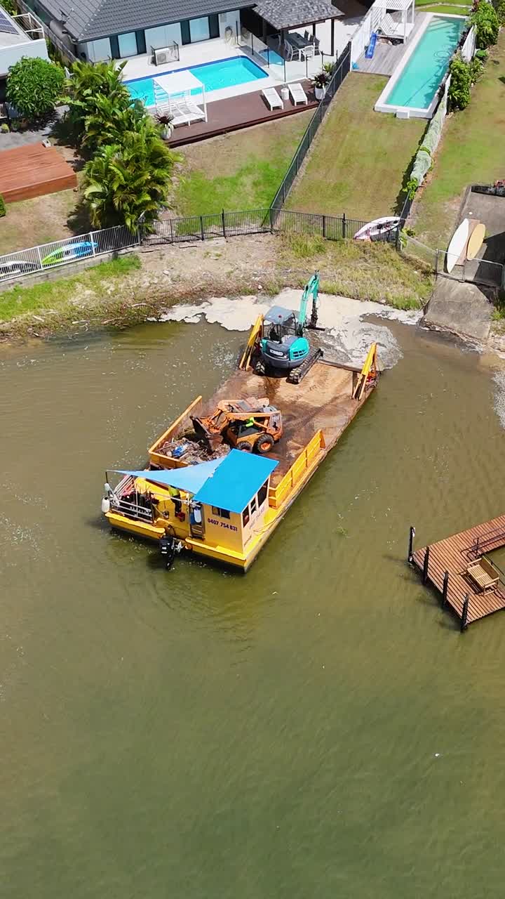 imágenes de drones capturan una barcaza y una grúa trabajando en un canal cerca de casas de lujo con piscinas