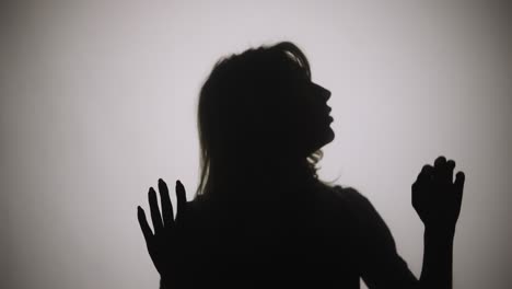 silhouette of woman emerges from smoke and touches glass with her palms - silhouette of woman emerges from smoke and touches glass with her palms. woman examines glass and slides her hands over it with interest. model poses in dark studio with yellow soft lights in background. close up