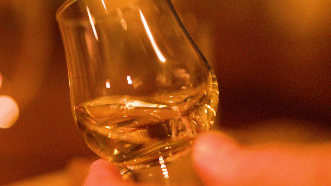 Close-up of hand swirling whisky glass, golden liquid, soft focus, warm ambient lighting, shallow depth