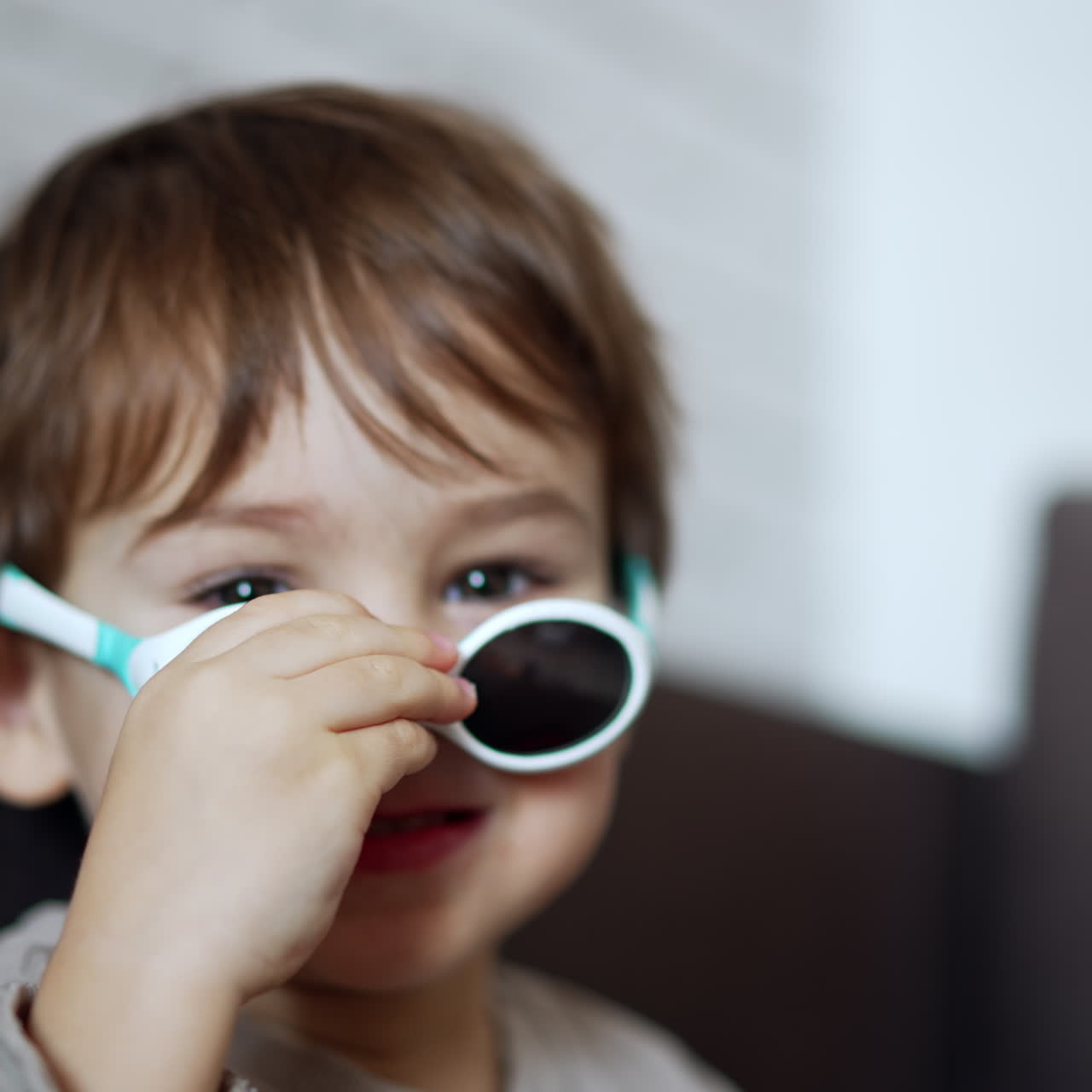 Bellissimo bambino caucasico si toglie e rimette gli occhiali da sole. Adorabile ritratto ravvicinato di bambino