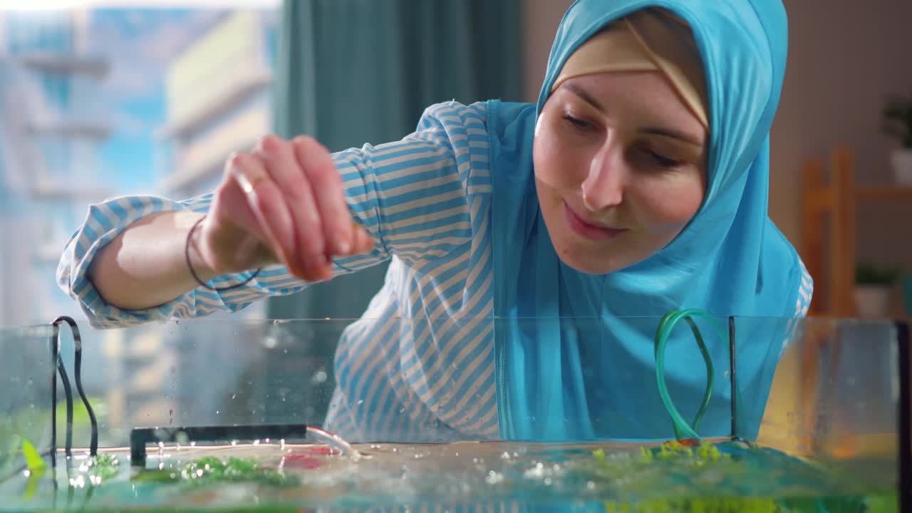 una mujer musulmana con un pañuelo nacional alimenta a los peces en un acuario en casa de cerca