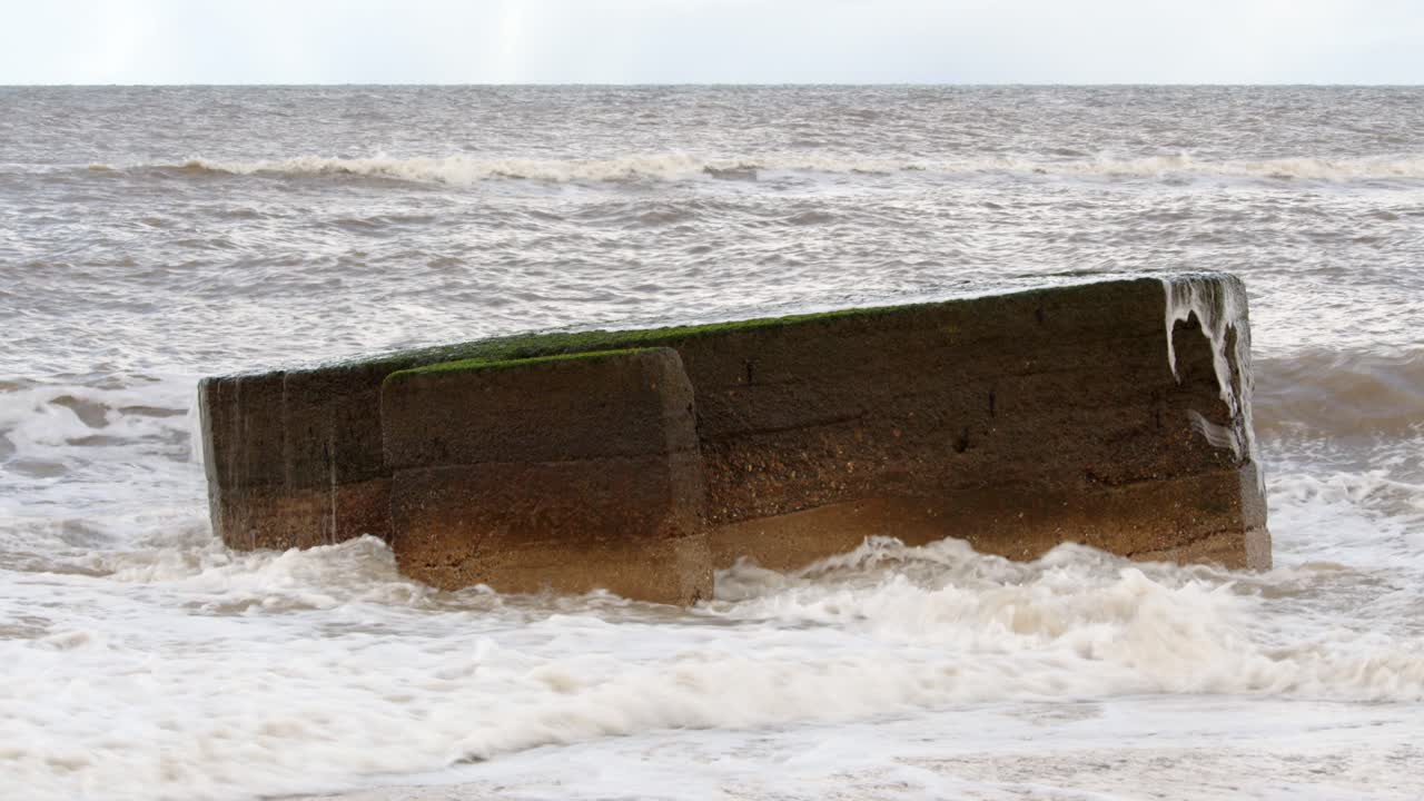 Waves breaking over the top of a World War II century pillar box on the Hemsby beach