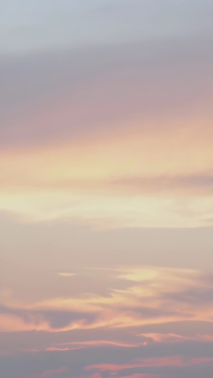 Vertical video: Shifting layered clouds deepening as sun sinking at dusk with blue gold pink bands