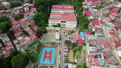 the aerial shot captures the layout of san agustin neighborhood, highlighting the school, colorful houses, and nearby sports court surrounded by parked vehicles. a vibrant community scene unfolds.