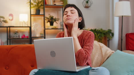 mujer independiente cansada sentada en el sofá usando una computadora portátil sufriendo de dolor de cabeza problema de tensión migraña