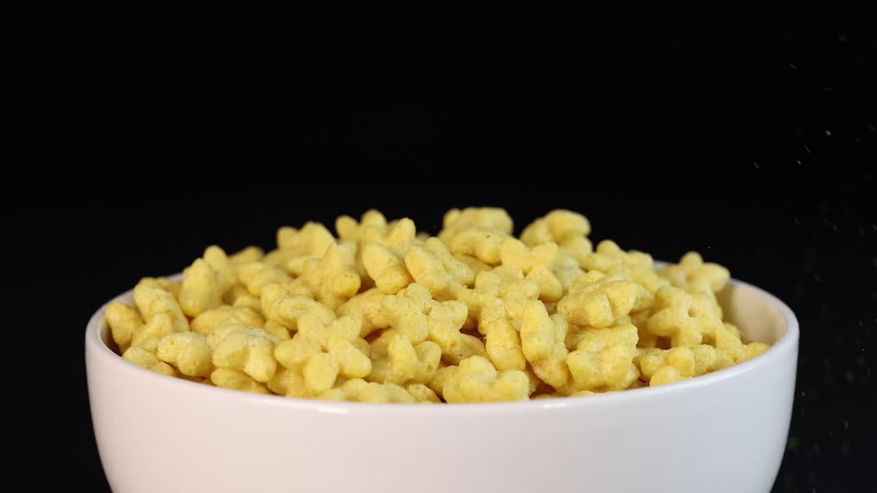 Yellow cereal pieces cascade into a white bowl, set against a dark backdrop, creating a dynamic and vibrant visual