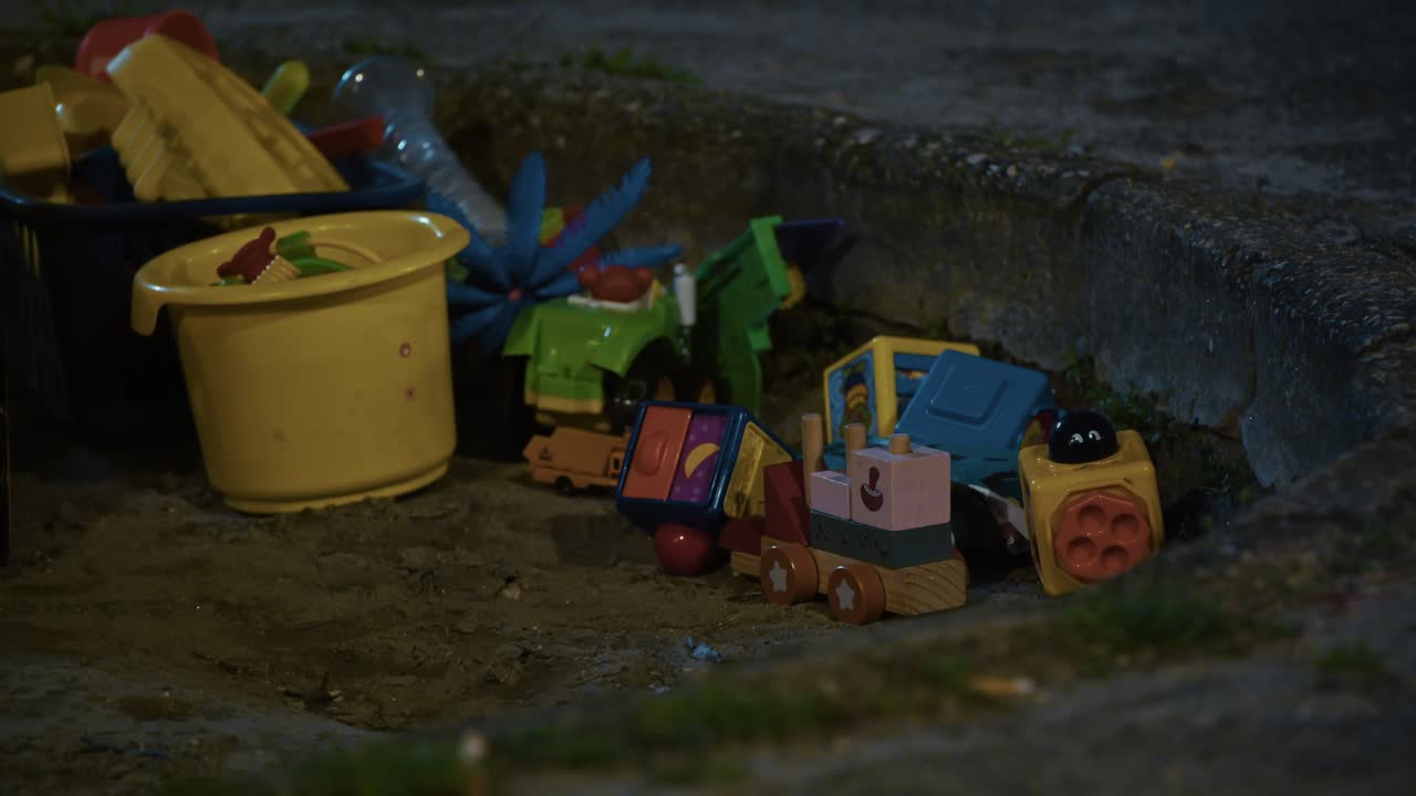 Colorful toys left in Zagreb sandbox at night under soft artificial lighting