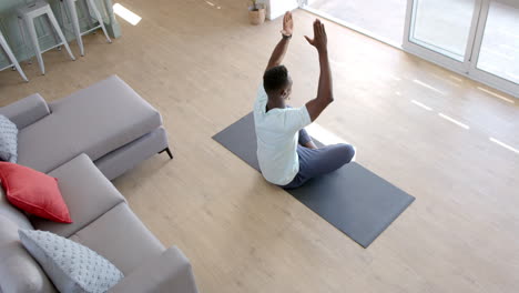 hombre afroamericano concentrado practicando meditación de yoga en la sala de estar soleada, cámara lenta