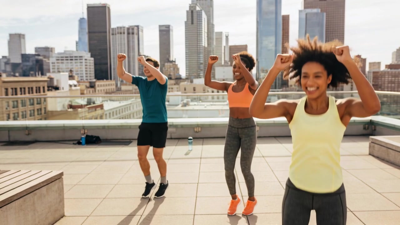 Jumping woman in yellow tank after cue, performing jumps on rooftop with water bottles for fitness