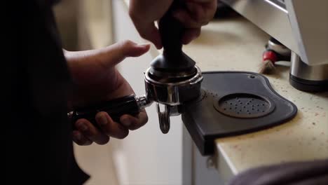 Crop-anonymous-barista-tampering-ground-aromatic-coffee-in-portafilter-on-tamper-mat-while-working-at-counter