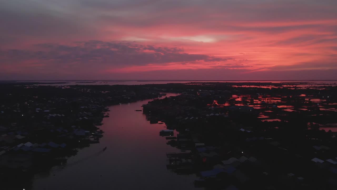Glødende reflekterende røde farver under en spektakulær solnedgang over en fiskerlandsby ved bredden af Tonle Sap-søen, Cambodja