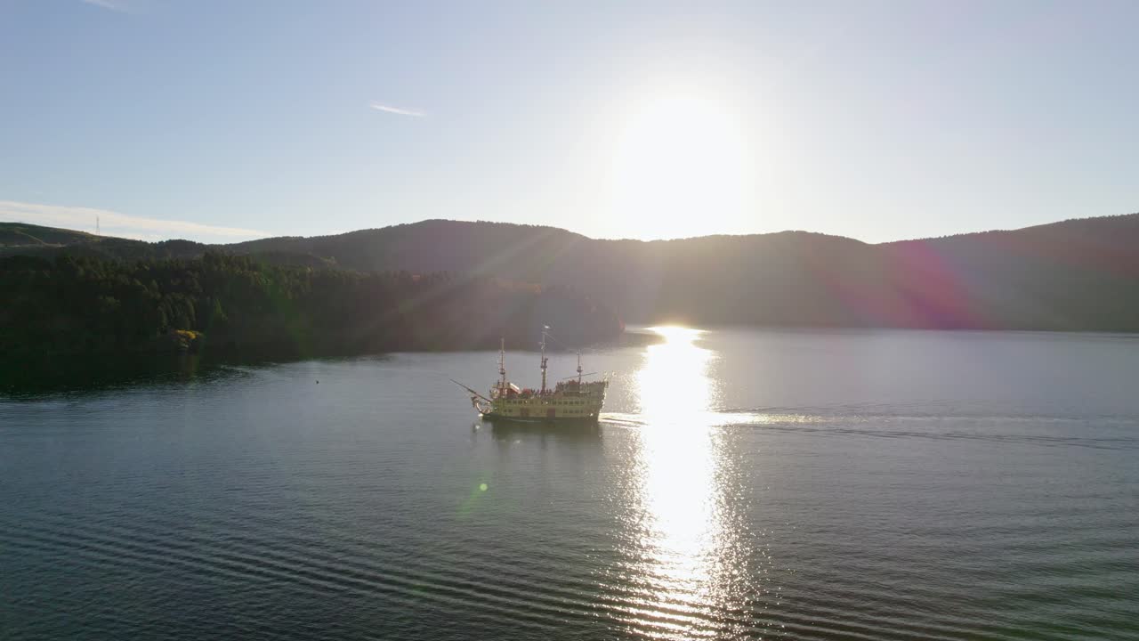 A still drone shot of the iconic Lake Ashi pirate ship gliding across calm waters under the sunlight in Hakone, Japan
