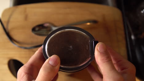 top down shot of a man placing the lid onto a coffee grinder and gridning cofee beans