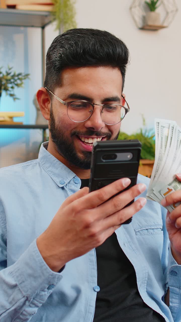Successful rich indian man use smartphone waving dollar bill money fan winning online lottery game