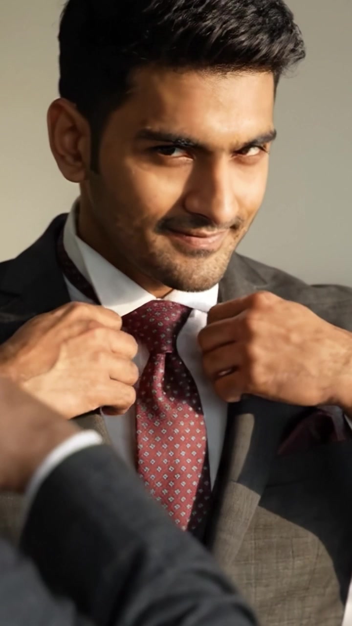 Un hombre seguro de sí mismo con un elegante traje que muestra sofisticación y moda moderna, perfectamente complementado con corbata y pañuelo de bolsillo para un look refinado.