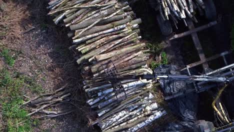 Top-down-aerial-view-of-a-tractor-using-a-grab-to-load-a-stack-of-wood-lengths-onto-the-trailer,-drone-movement-following-grab