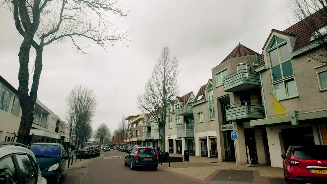 An urban street scene with buildings, vehicles, and a cyclist on an overcast day