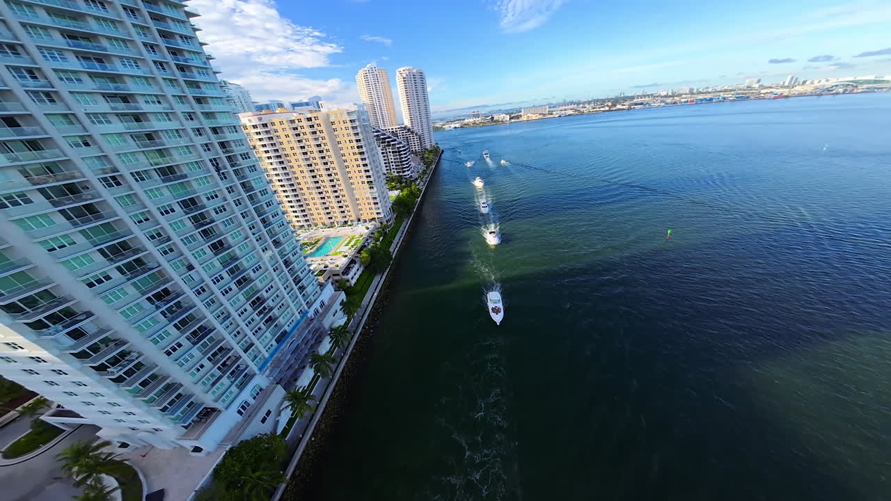 Yachts sail along the waterfront of a modern American city, FPV drone flies above the luxurious buildings in the beautiful residential area.